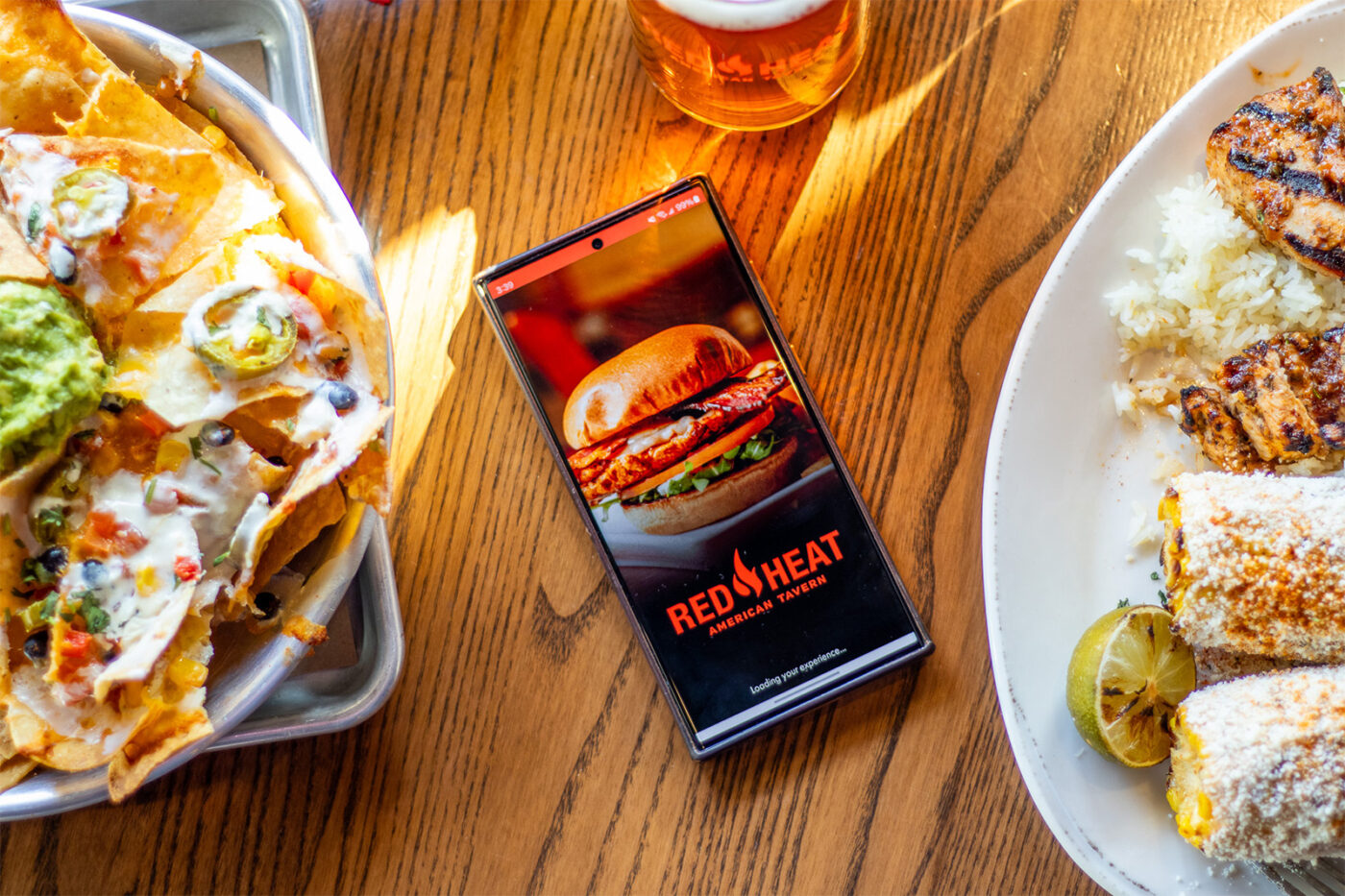 Red Heat American Tavern app on phone with nachos and corn on the side