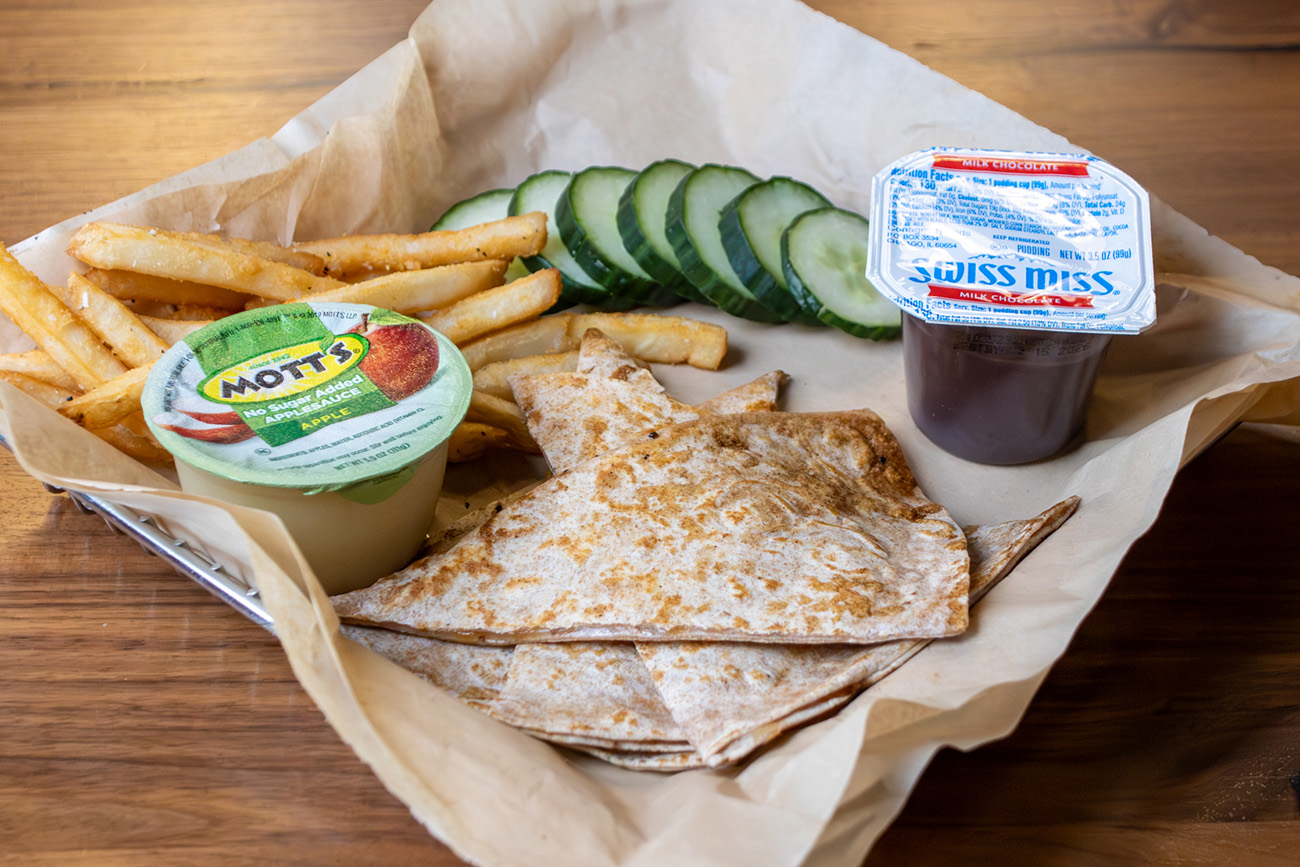 Kids Meal with a quesadilla, side of sliced cucumbers, apple sauce, fries and a pudding cup