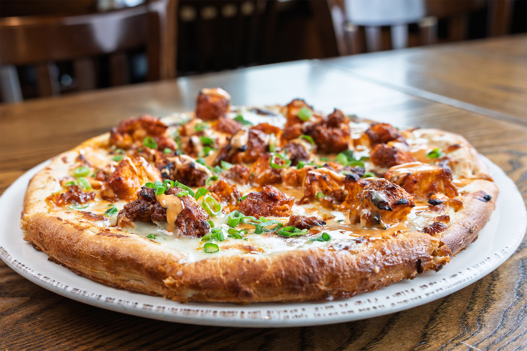 Buffalo chicken pizza with crispy buffalo chicken, blue cheese sauce, sriracha aioli, and scallions
