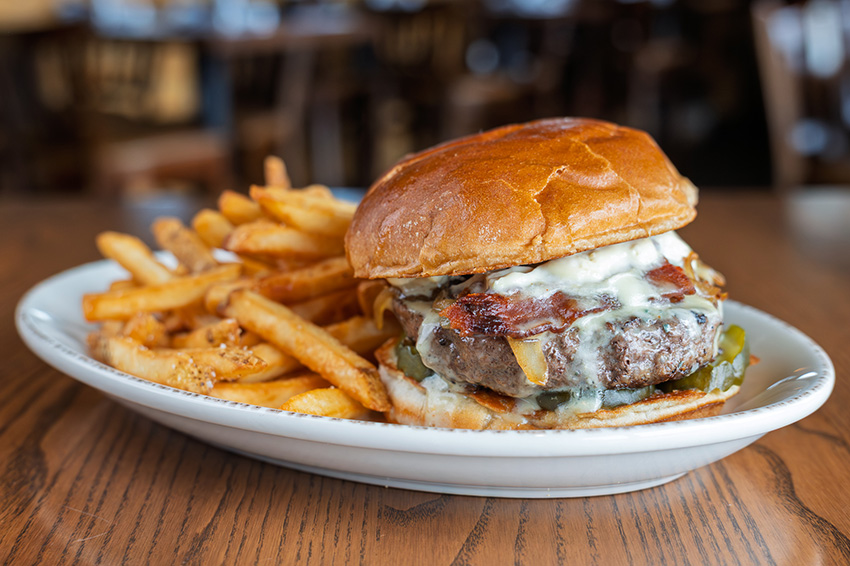 Tavern Burger served with applewood-smoked bacon, house-made blue cheese cream sauce, caramelized onions, and roasted garlic aioli with french fries on the side
