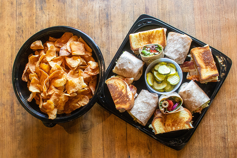 Catering sandwich platter featuring the mediterranean wrap, chicken caesar wrap, grilled pesto melt, grilled chicken sandwich, and a side of house-made chips