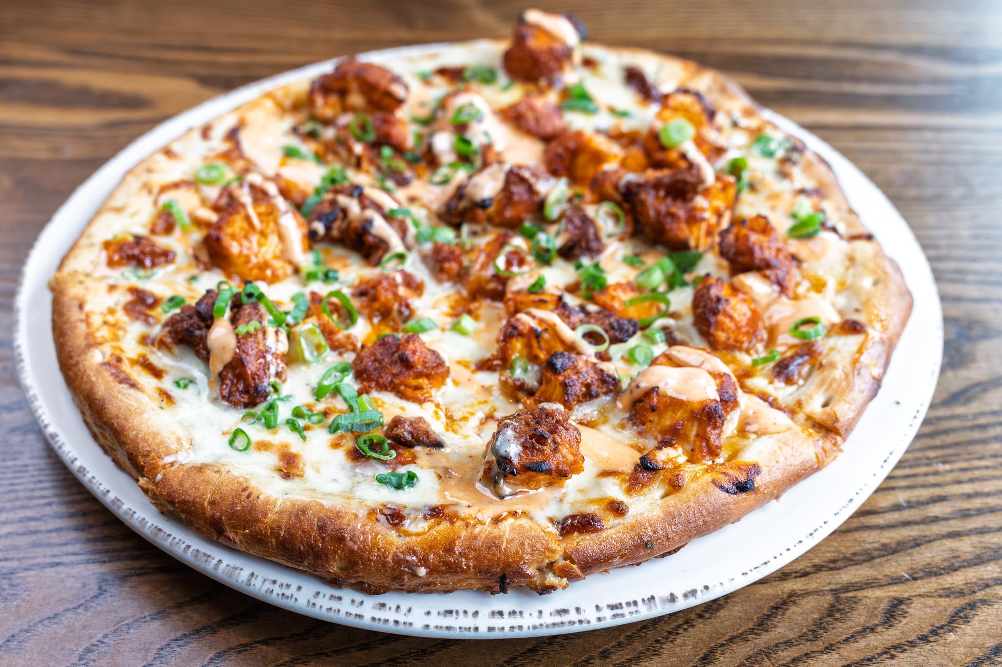 Buffalo Chicken Pizza made with crispy buffalo chicken, blue cheese sauce, sriracha aioli, scallions. Gluten free crust available on request.