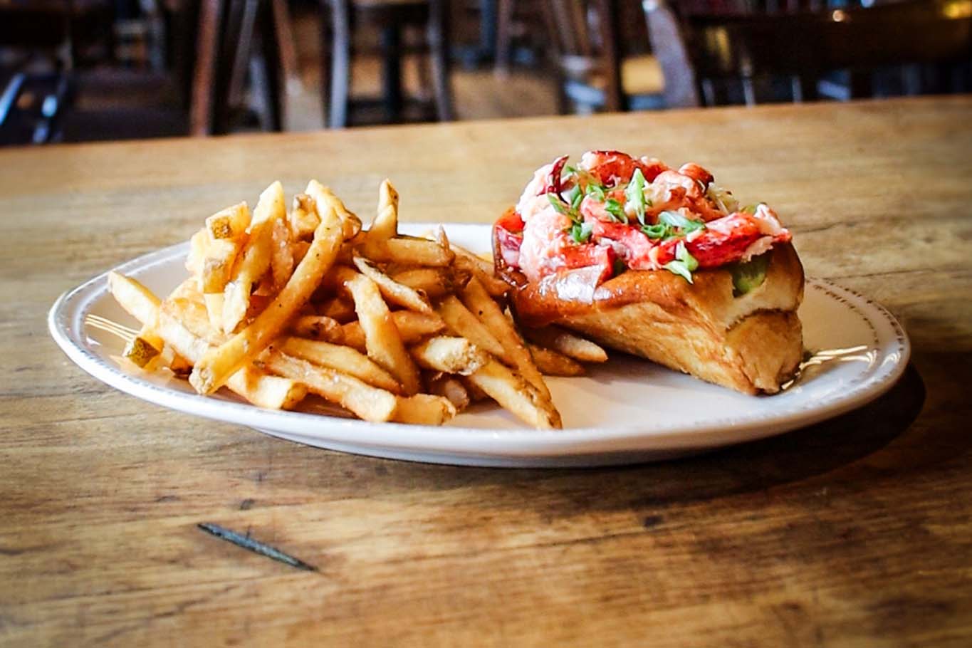 A lobster roll on a plate with french fries