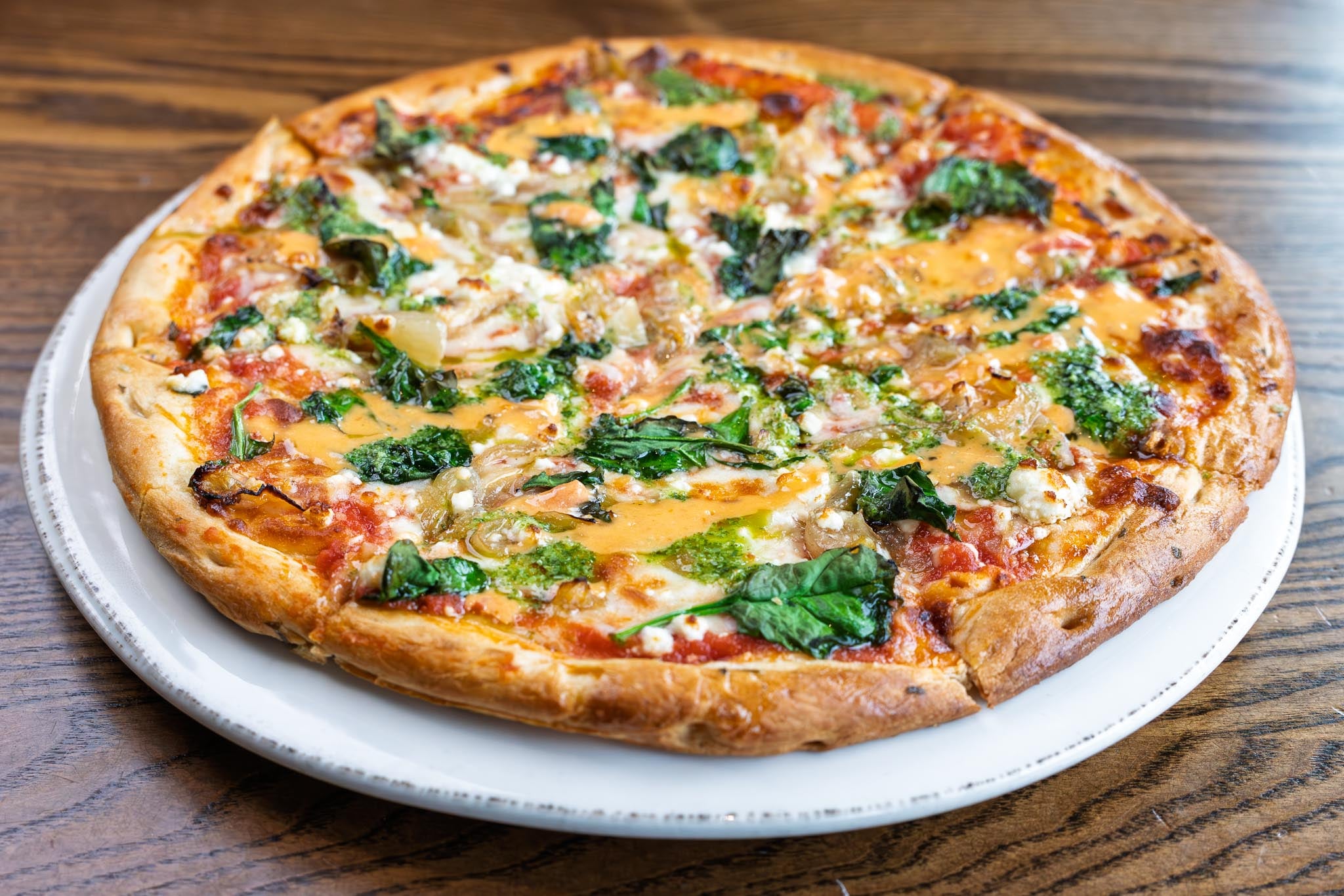 Mediterranean pizza made with caramelized onions, spinach, feta cheese, house-made tomato sauce, sun-dried tomato beurre blanc, pesto drizzle. Gluten free crust available on request